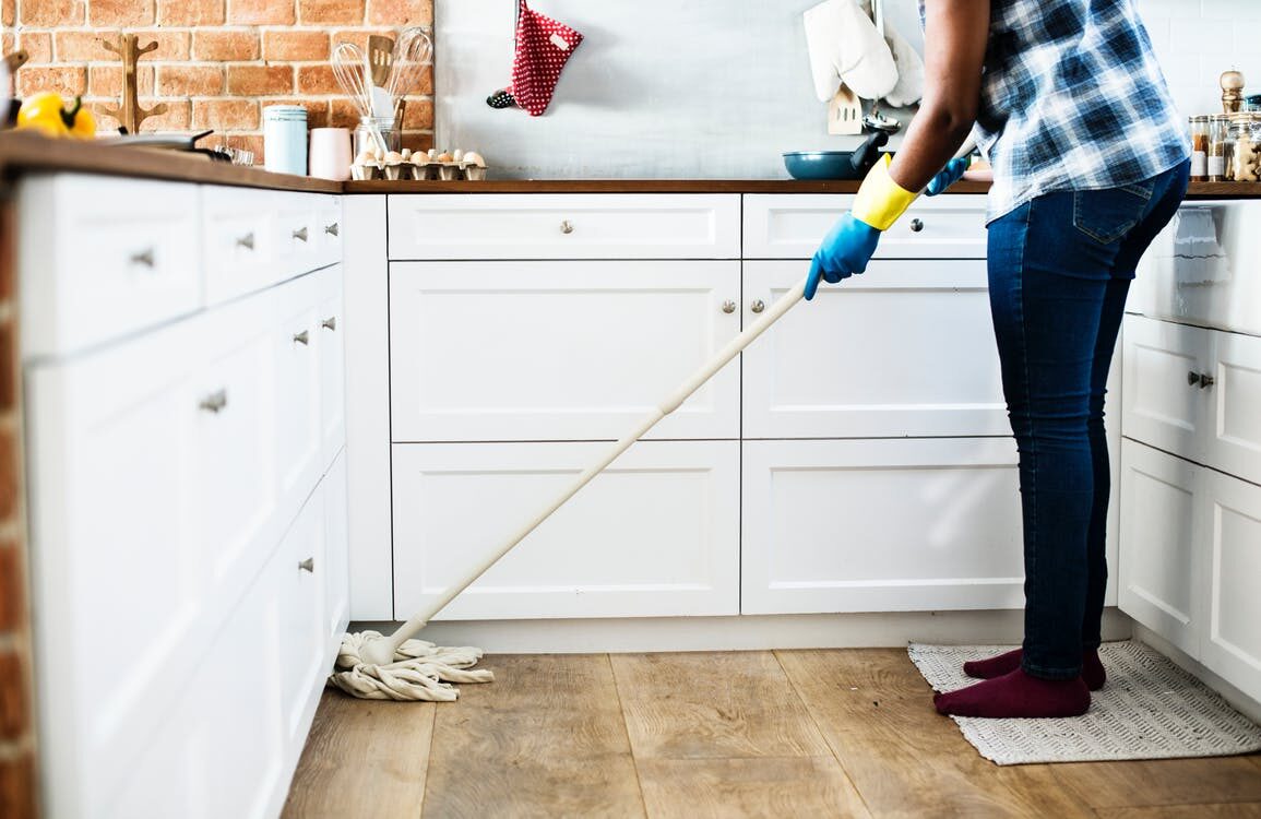 Person wearing jeans and striped socks cleaning a white kitchen countertop with a spray bottle and cloth
