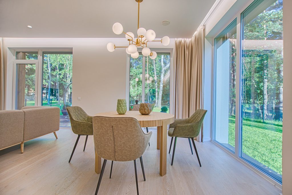 Dining area with a modern chandelier, round table, green chairs, and large windows with natural light