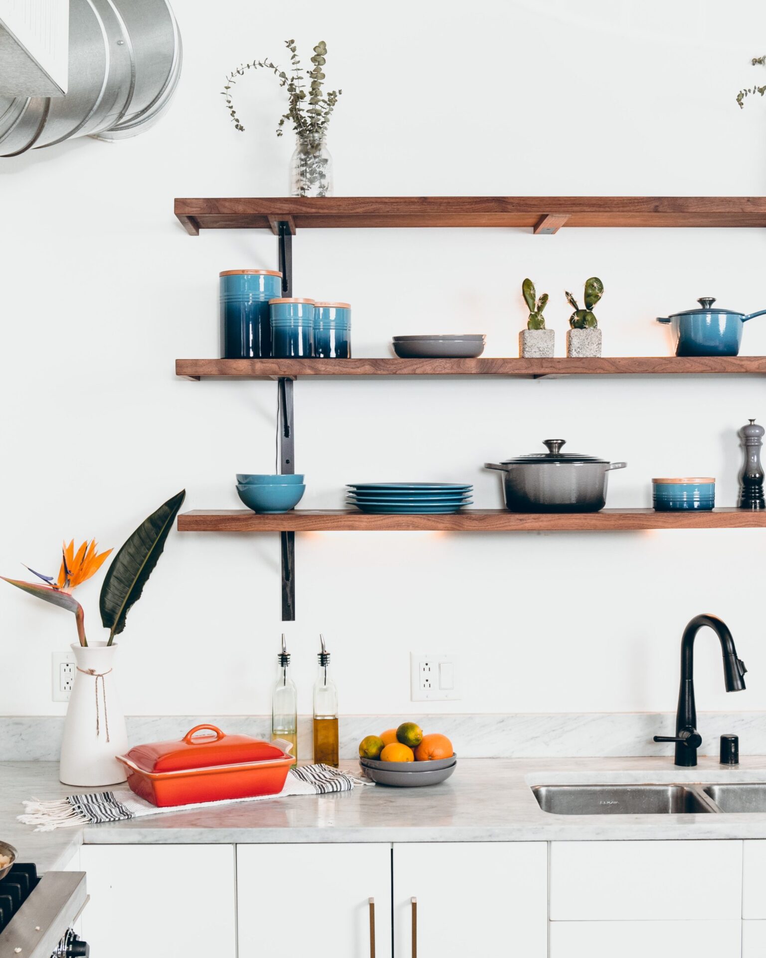 Modern kitchen featuring open wooden shelves, dishes, plants, and a white counter with a black faucet