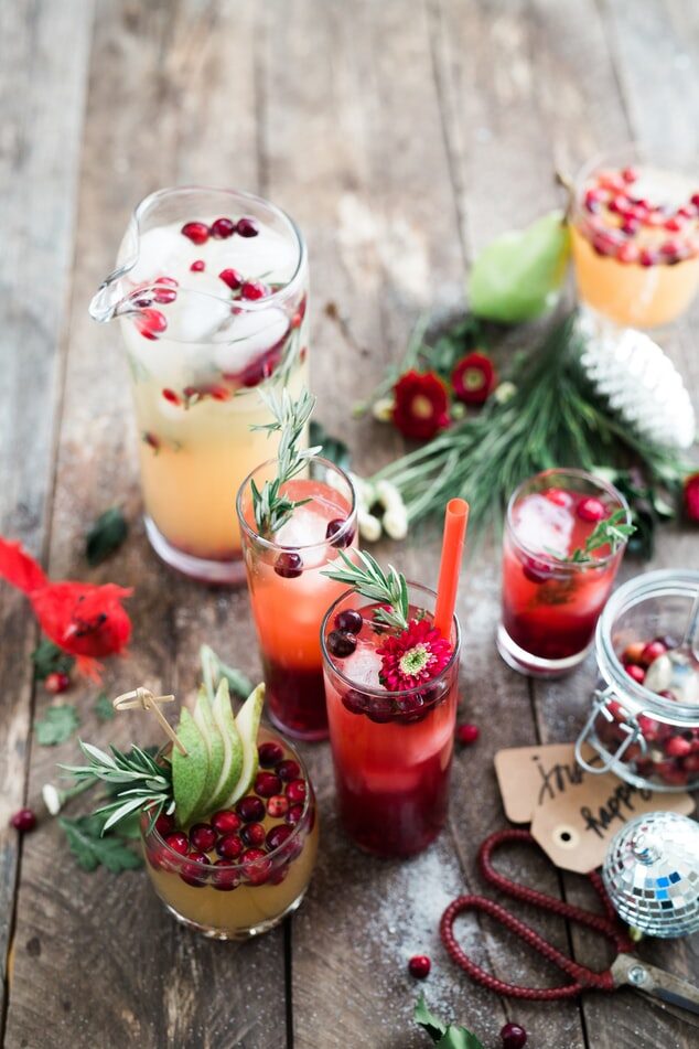Assorted holiday cocktails with cranberries and festive garnishes on a rustic wood table