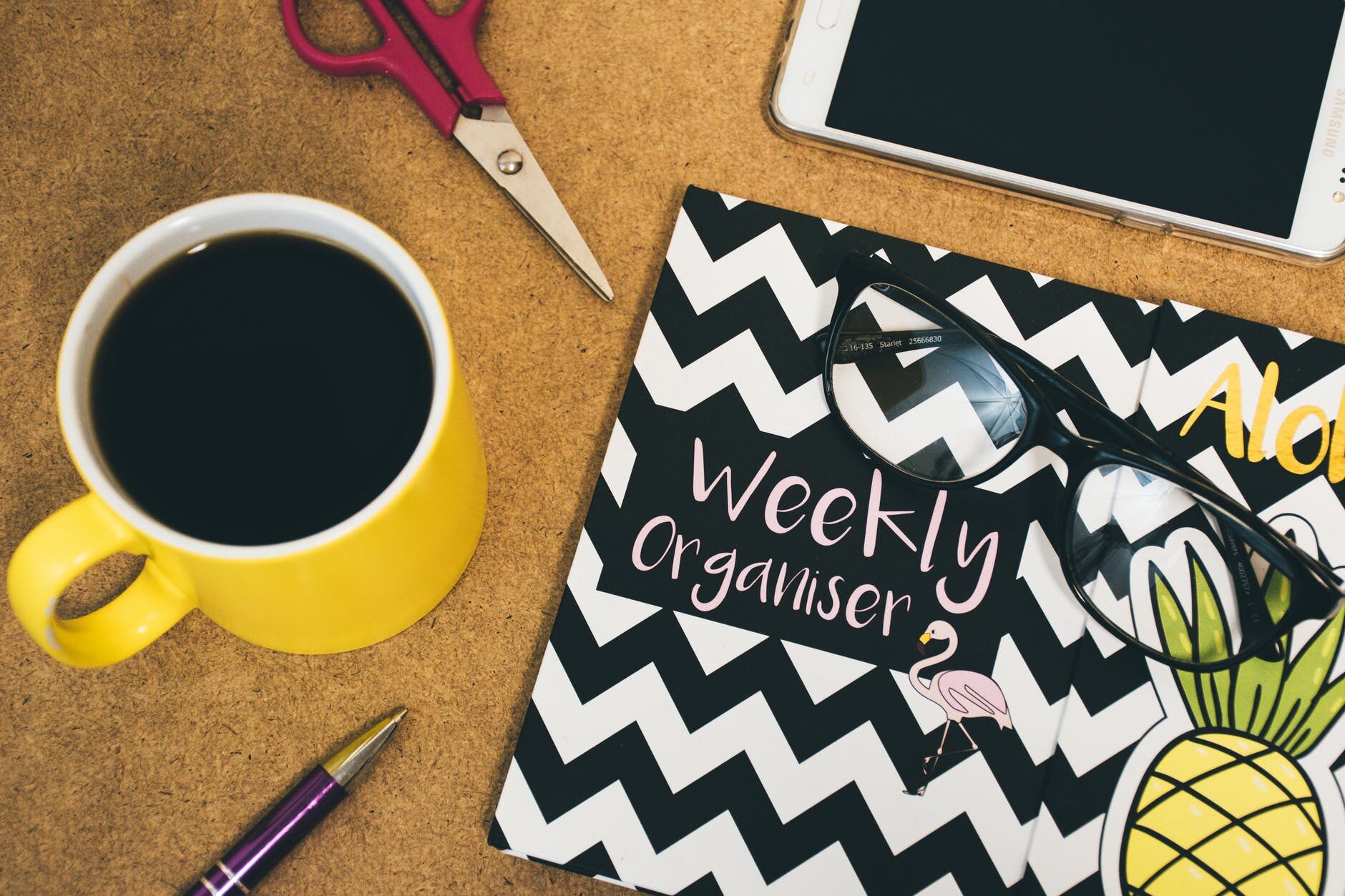 Yellow coffee mug, pen, and a black-and-white weekly organizer on a wooden desk