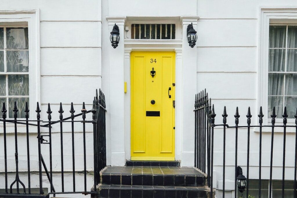 Bright yellow front door of a home with a wall sconce light and black iron railing