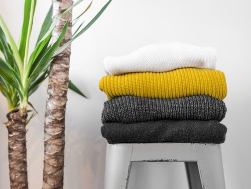 Stack of colorful folded throws and cushions next to a green houseplant