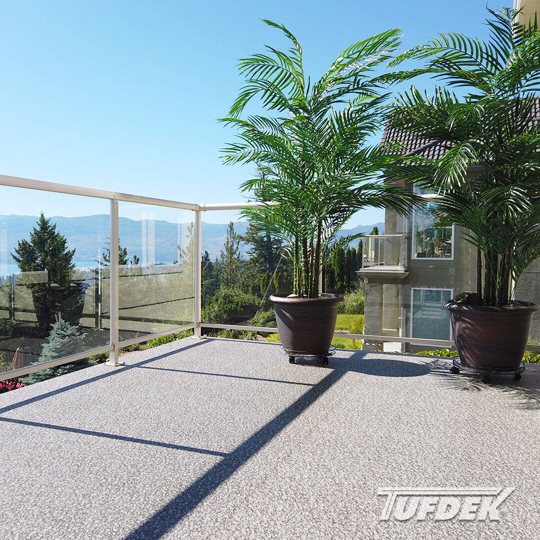 Outdoor balcony with weather-resistant flooring, potted palm plant, and glass railing overlooking scenic mountains and blue sky.